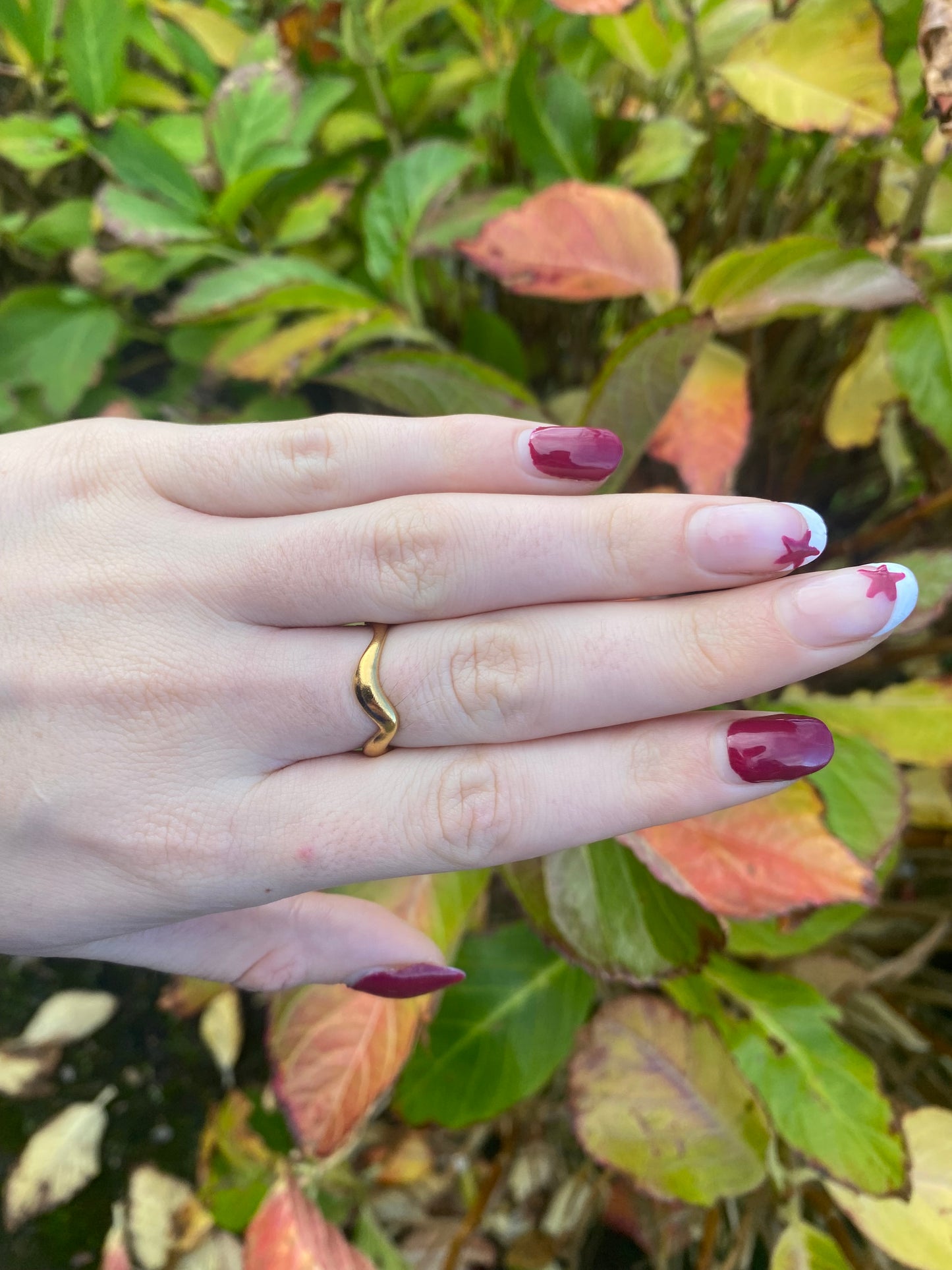 Hand wearing a gold ring with a blurred green leafy background